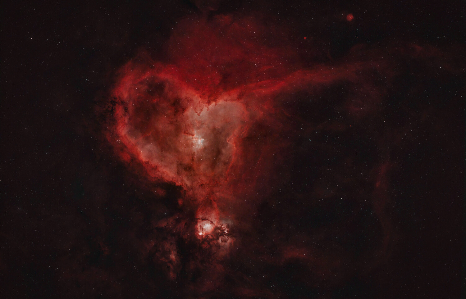 Glowing red heart-shaped emission nebula against a dark starfield, with a bright star cluster at its lower edge.