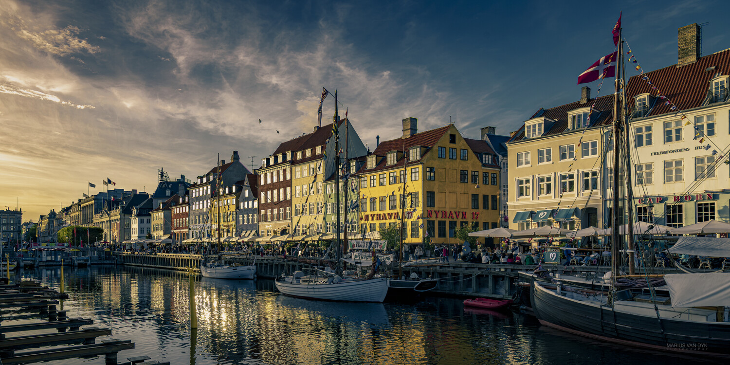 Colorful waterfront buildings and sailboats along a European harbor at golden hour