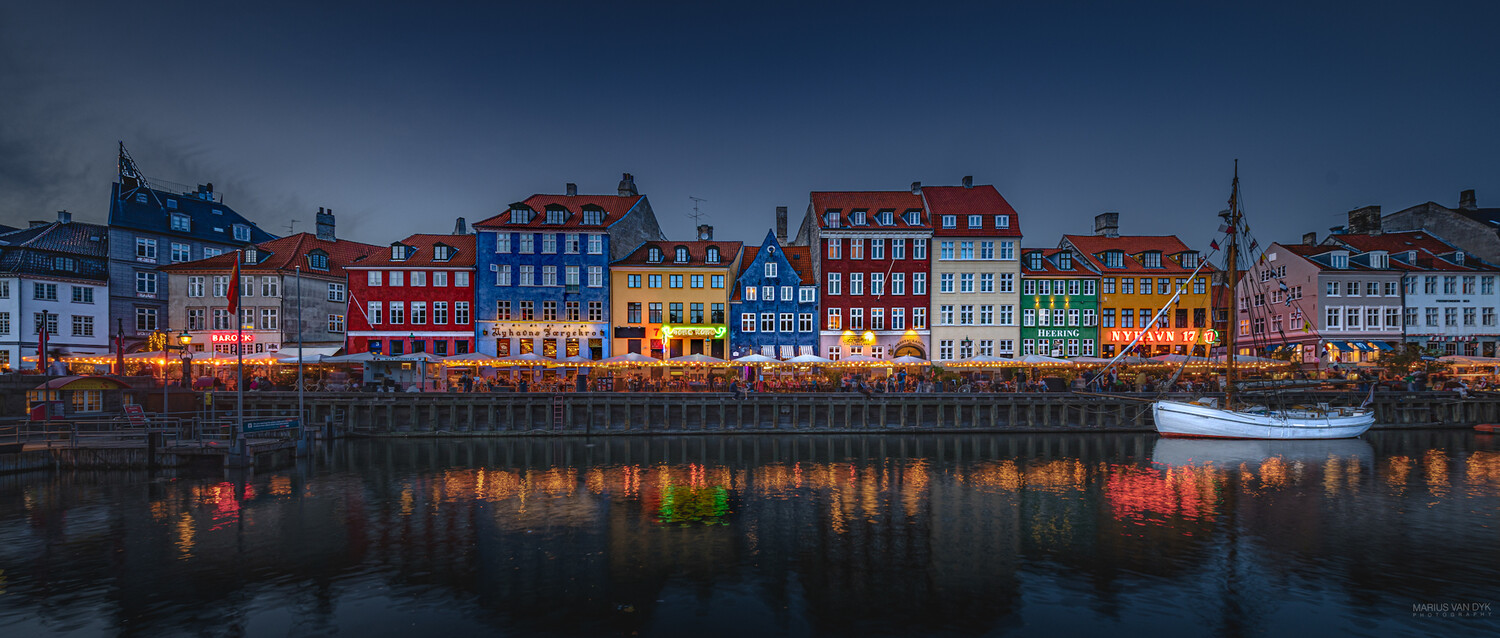 Colorful waterfront buildings reflected in calm water at twilight with a moored boat