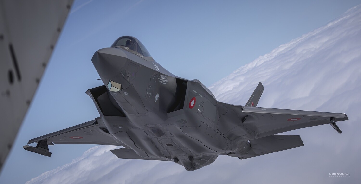 Military stealth fighter jet in flight photographed from another aircraft against blue sky