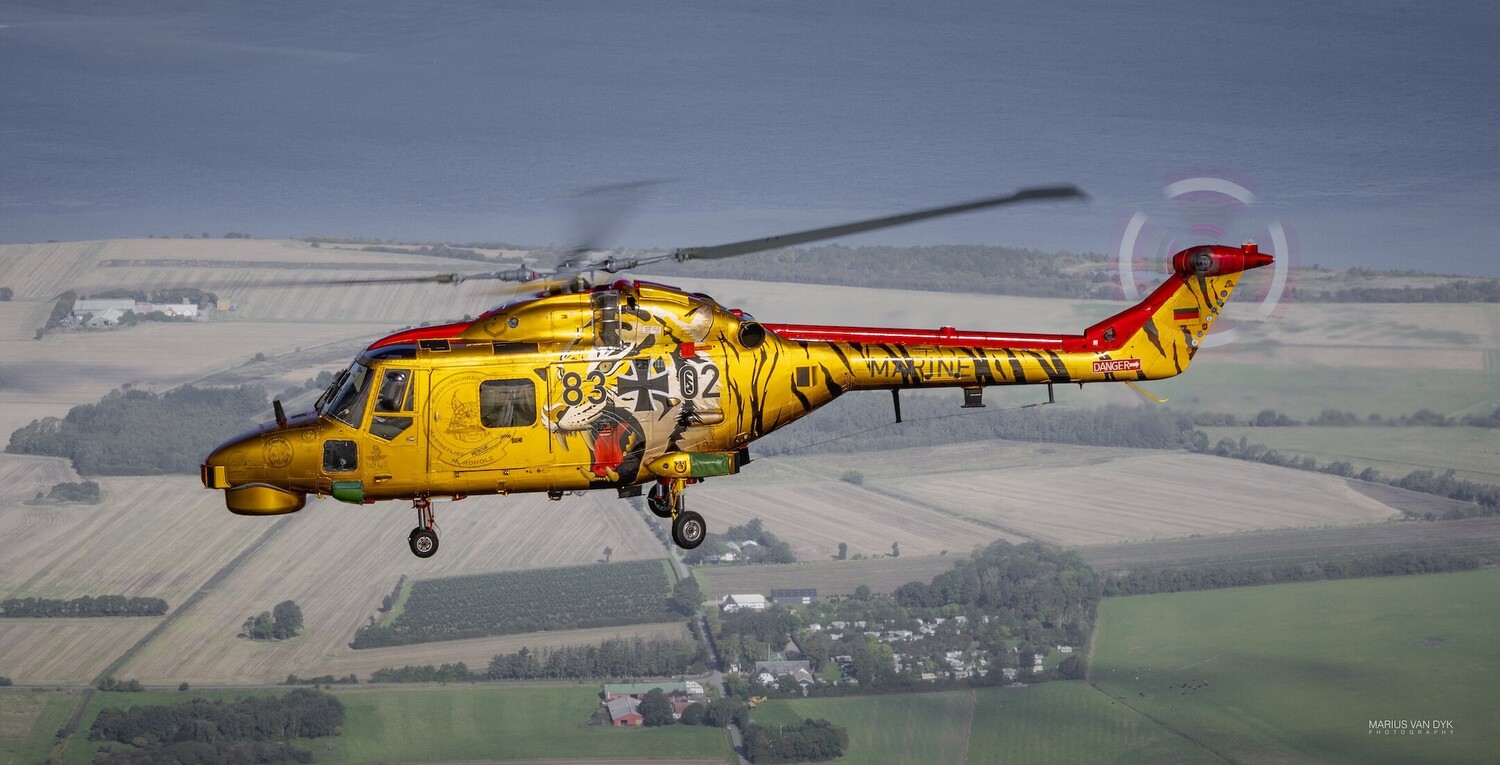 Yellow and red rescue helicopter in flight over agricultural landscape