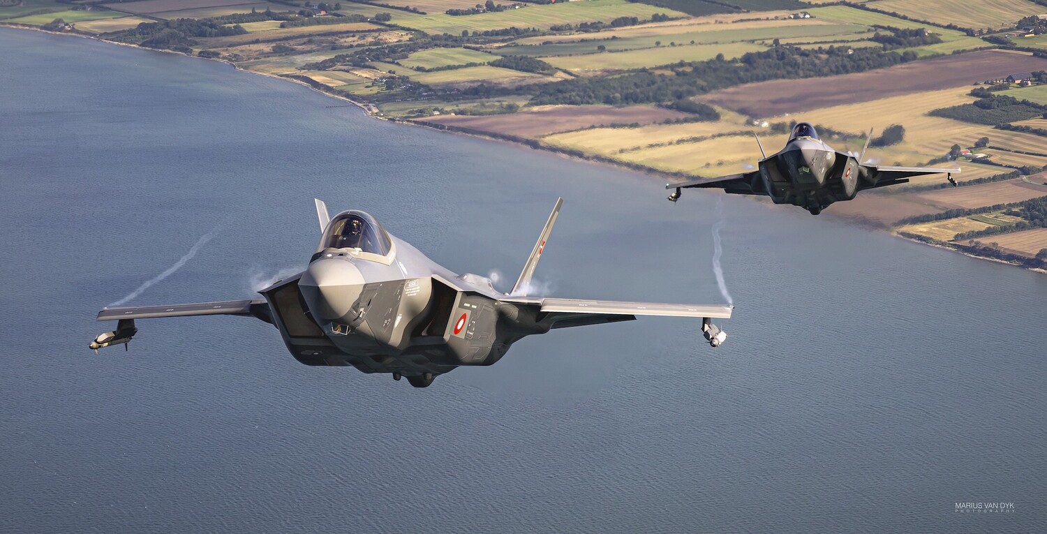 Two F-35 fighter jets in formation flying over coastal farmland