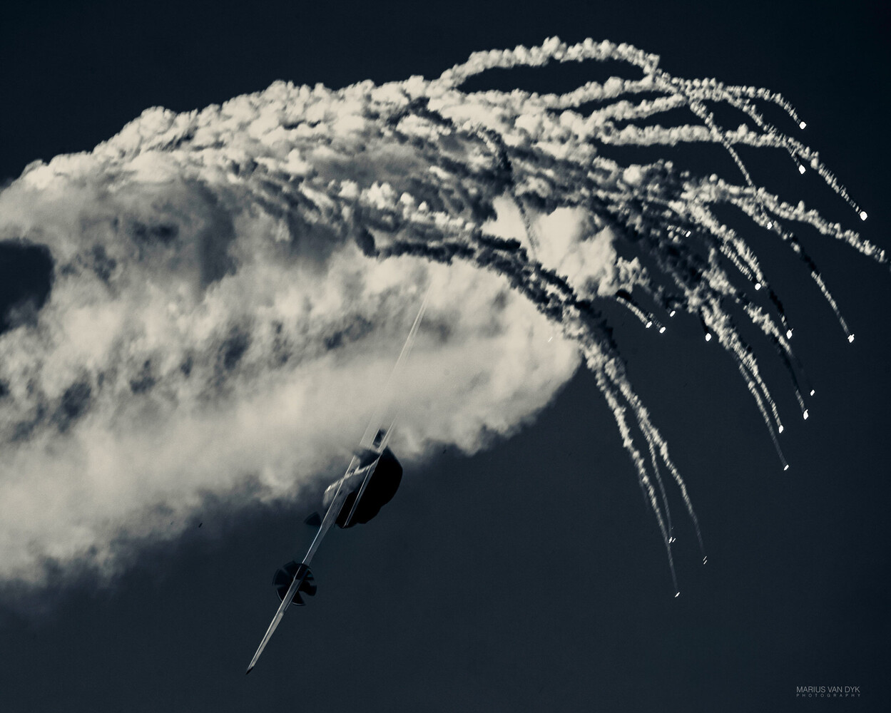 Military aircraft executing defensive flare deployment against dark sky
