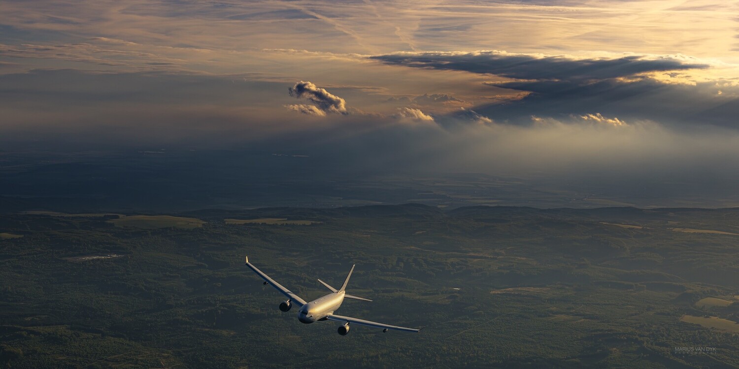 Commercial aircraft in flight during golden hour with dramatic cloudscape below