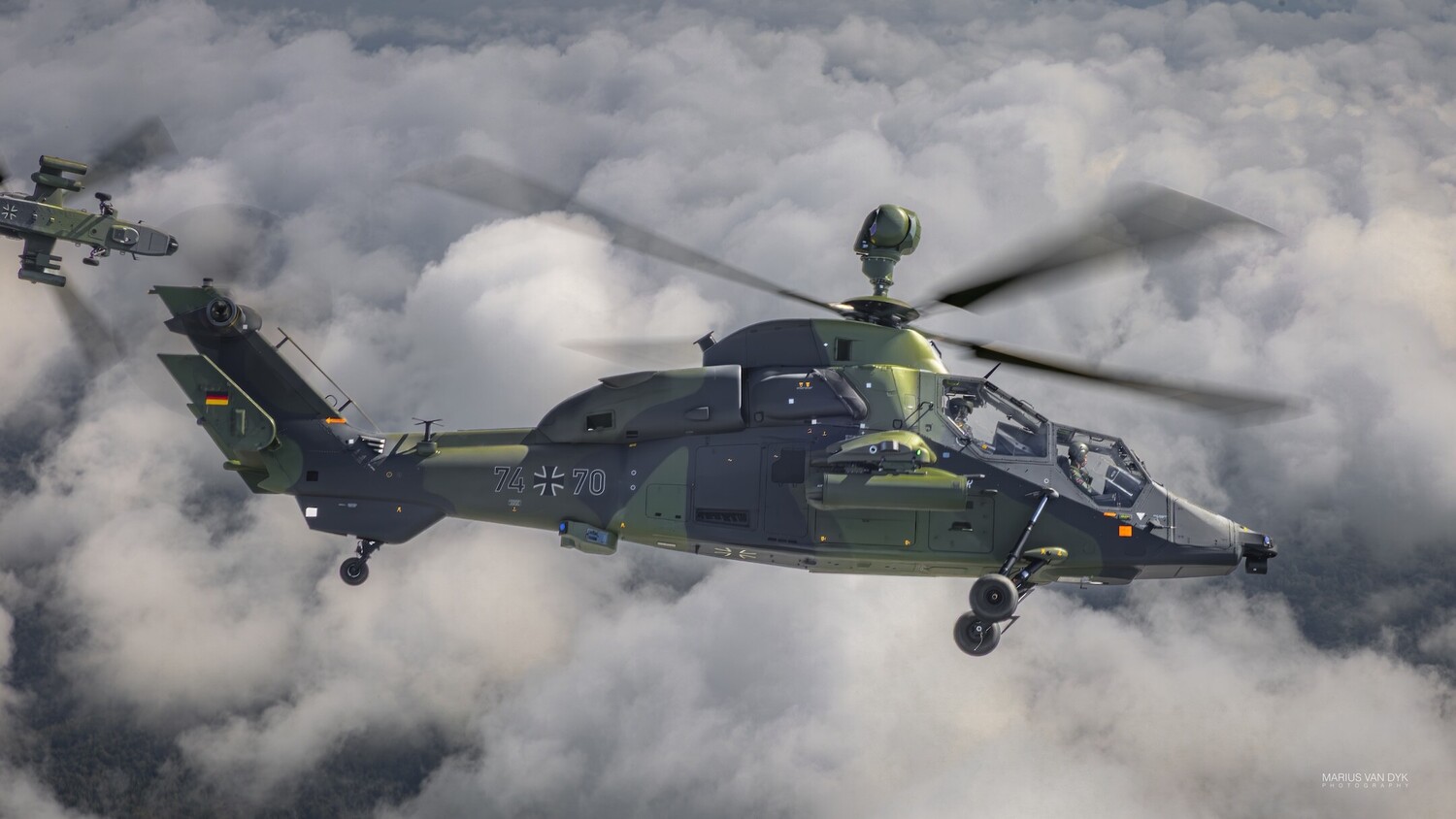 Military attack helicopter flying through clouds with another helicopter visible in the background