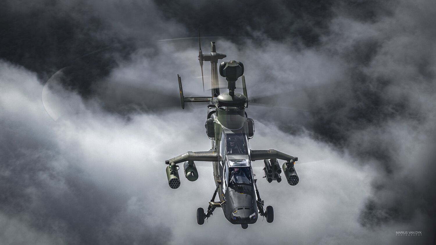 Military attack helicopter photographed from below against dramatic stormy clouds