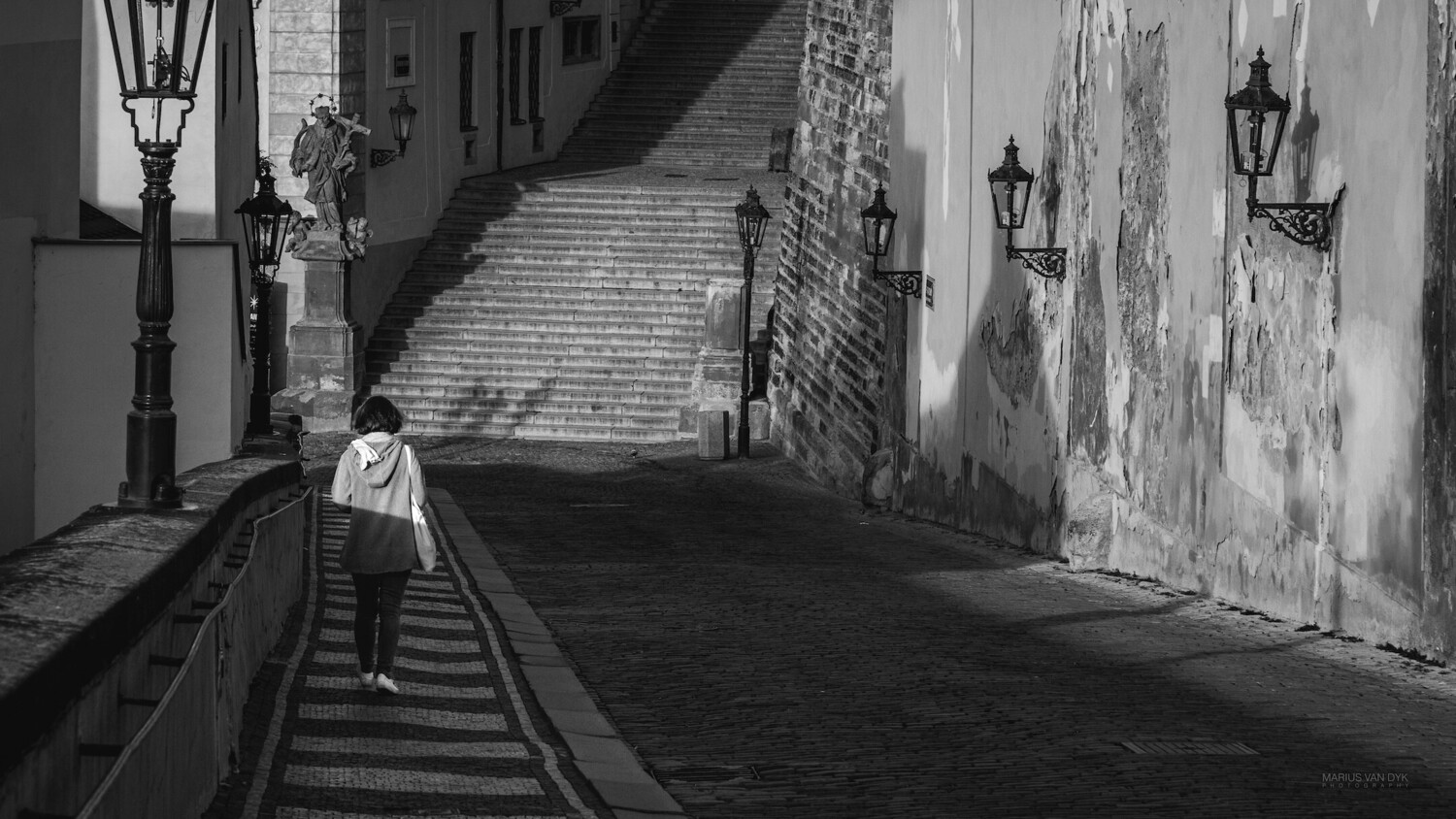 Solitary figure in white shirt walking down narrow European street with stairs and old buildings