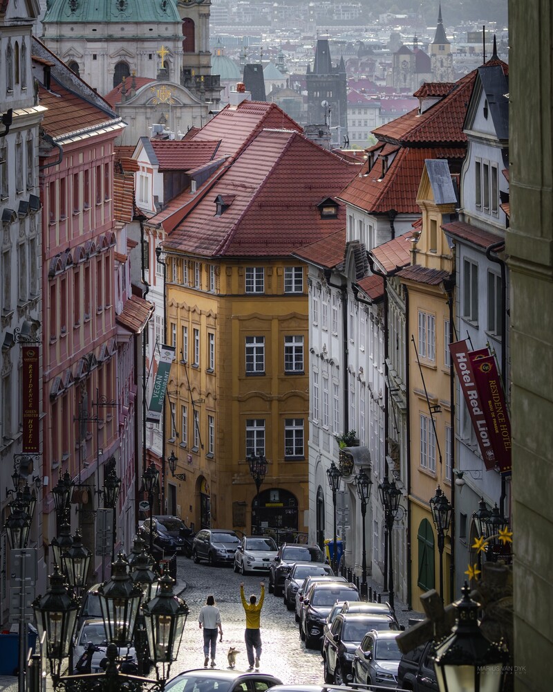 Narrow European street lined with colorful buildings descending toward a distant cityscape