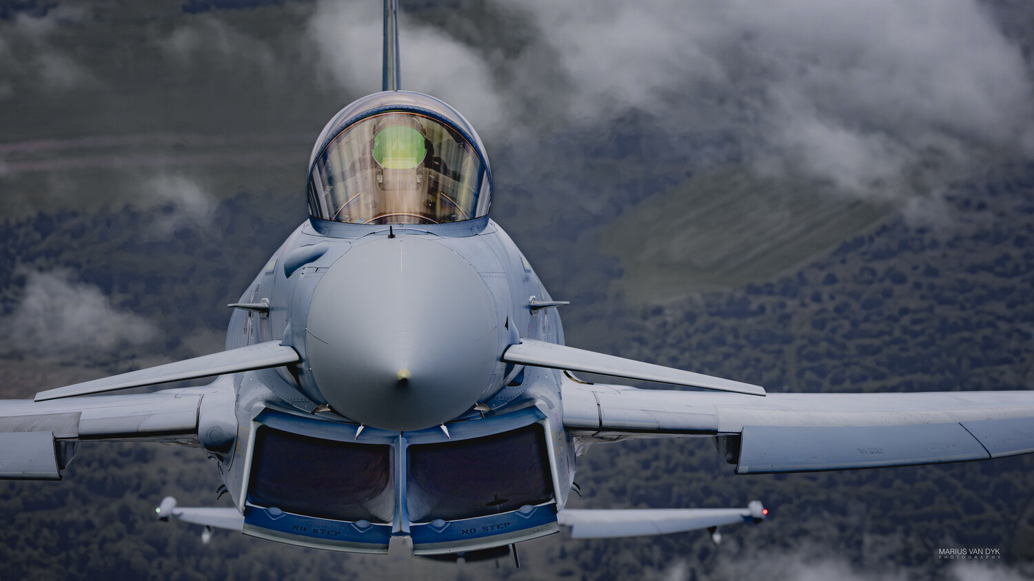 Front view of a military fighter jet in flight against a cloudy sky backdrop