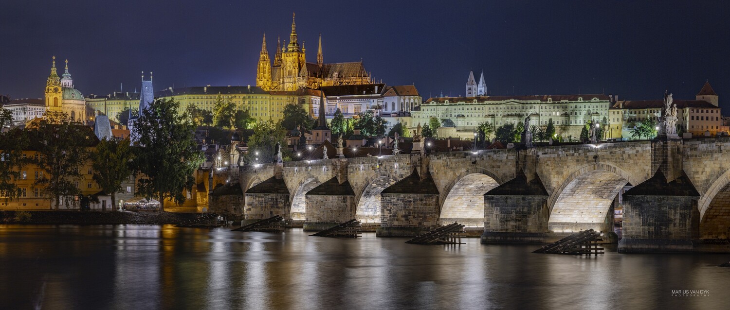 Charles Bridge spanning the Vltava River at dusk with Prague Castle illuminated on the hillside