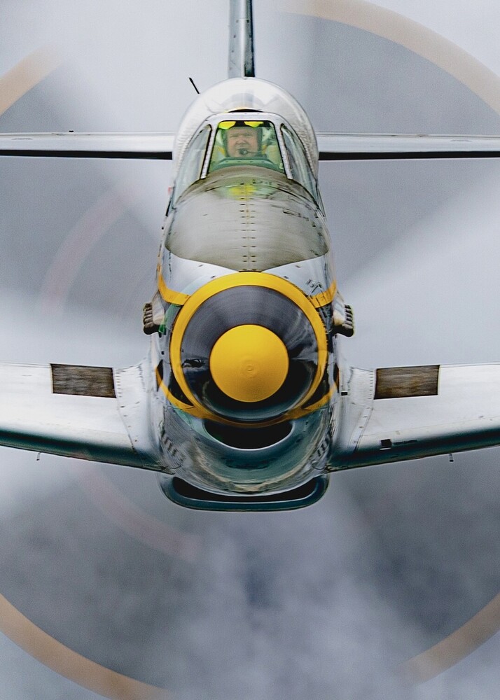 Head-on view of a military transport aircraft with yellow engine housing and open cockpit window