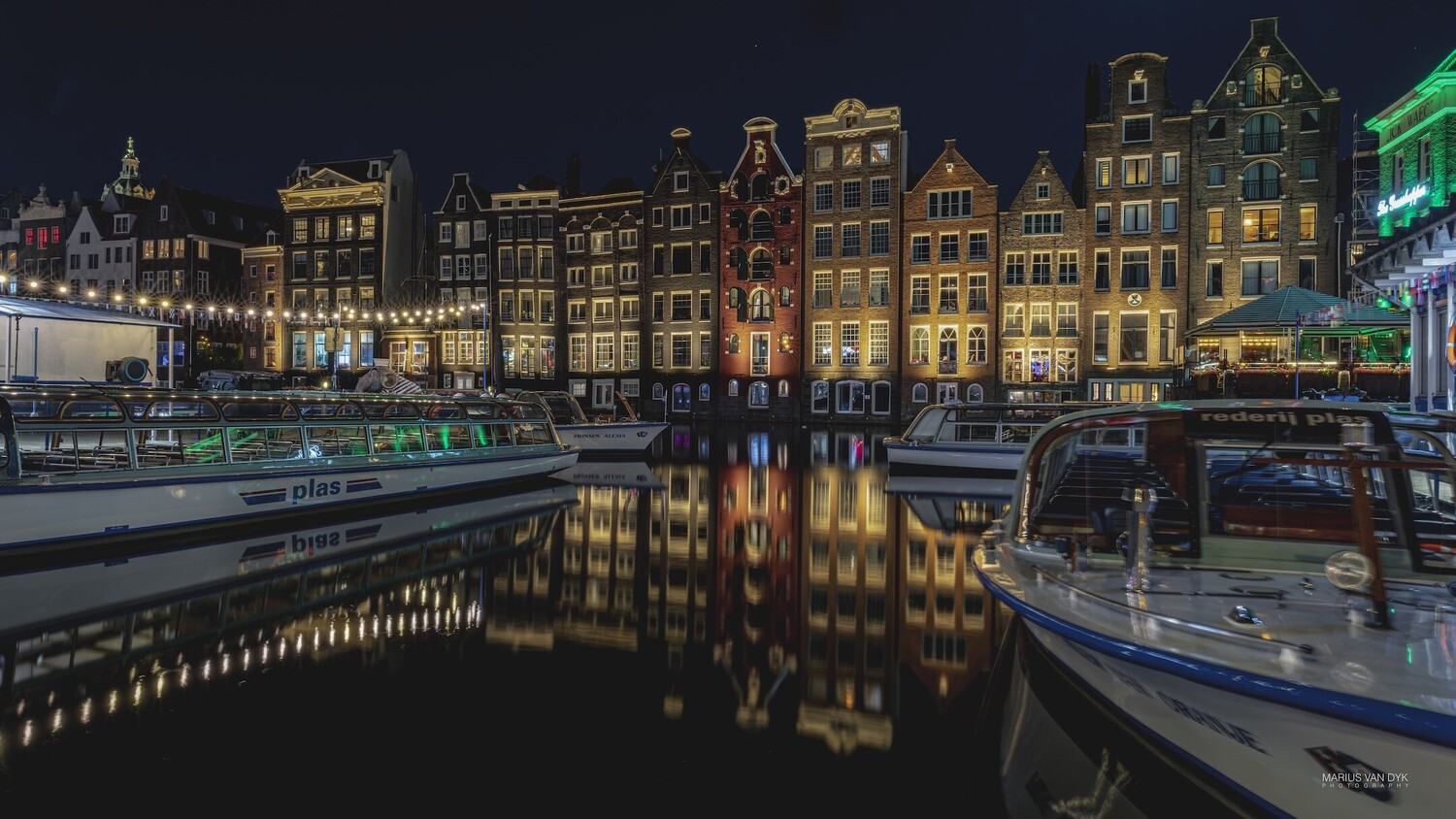 Historic waterfront buildings reflected in still canal water at night with illuminated facades and moored boats