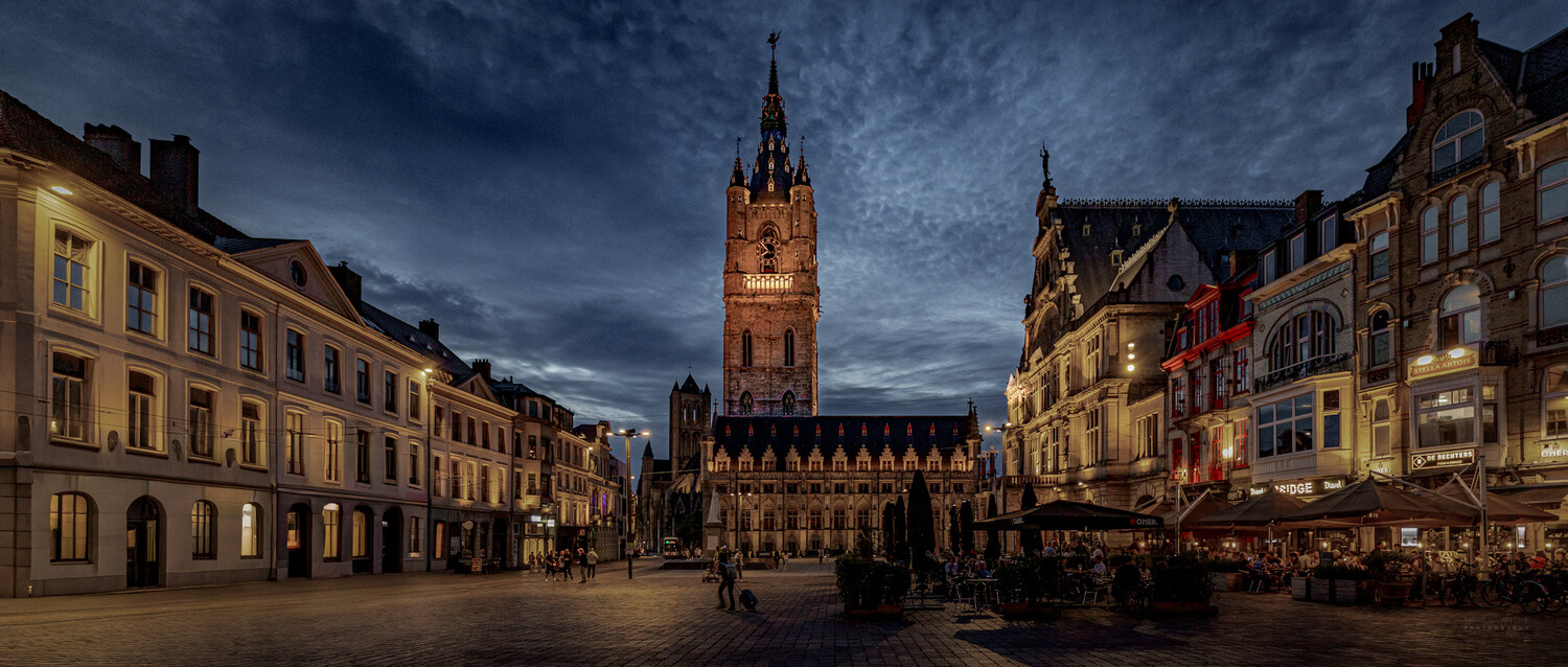 Illuminated medieval town square with central clock tower at twilight