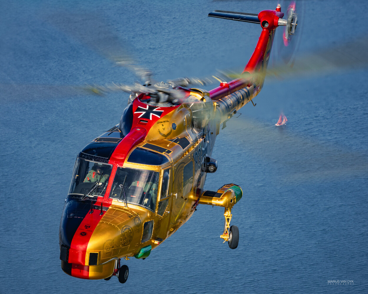 Red and yellow rescue helicopter hovering over blue water with deployed winch cable