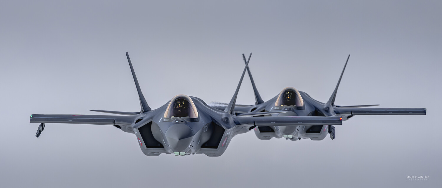 Two grey F-35 Lightning II fighter jets flying in close formation toward the camera against a pale, overcast sky