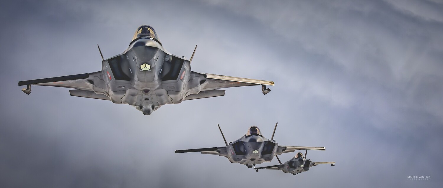 Three gray F-35 Lightning II fighter jets flying in formation against a cloudy gray sky, shot from below
