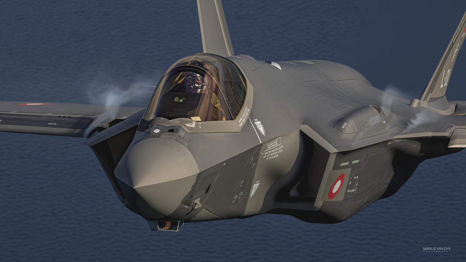 Grey F-35 Lightning II stealth fighter jet flying over dark blue ocean, nose and cockpit canopy in the foreground.