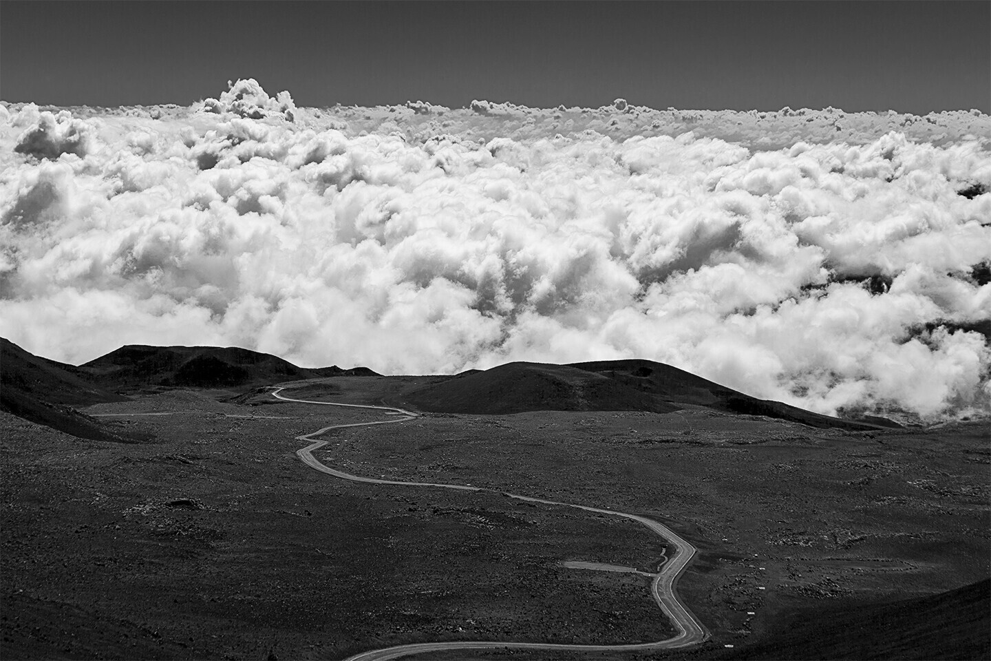 Dark volcanic landscape with winding path beneath towering sea of clouds