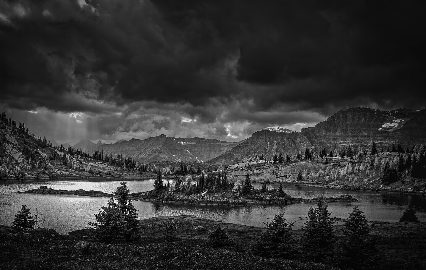 Dramatic black and white landscape of a forested alpine lake with stormy sky and mountain peaks