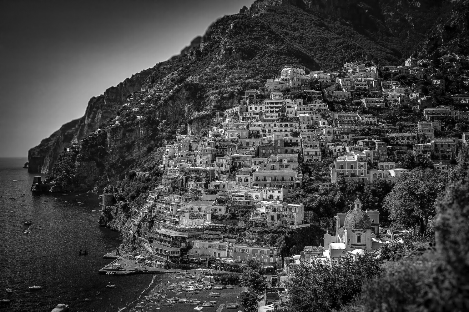 Densely stacked white buildings cascading down a steep coastal cliff in black and white