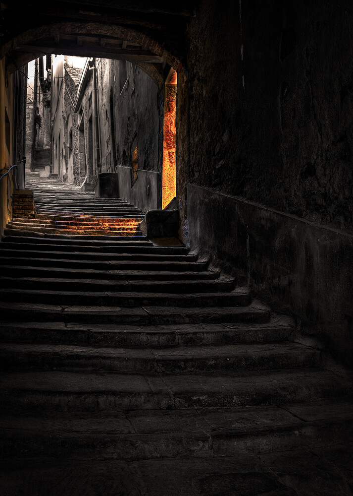 Dark stone staircase descending into shadows with warm light visible through a distant archway