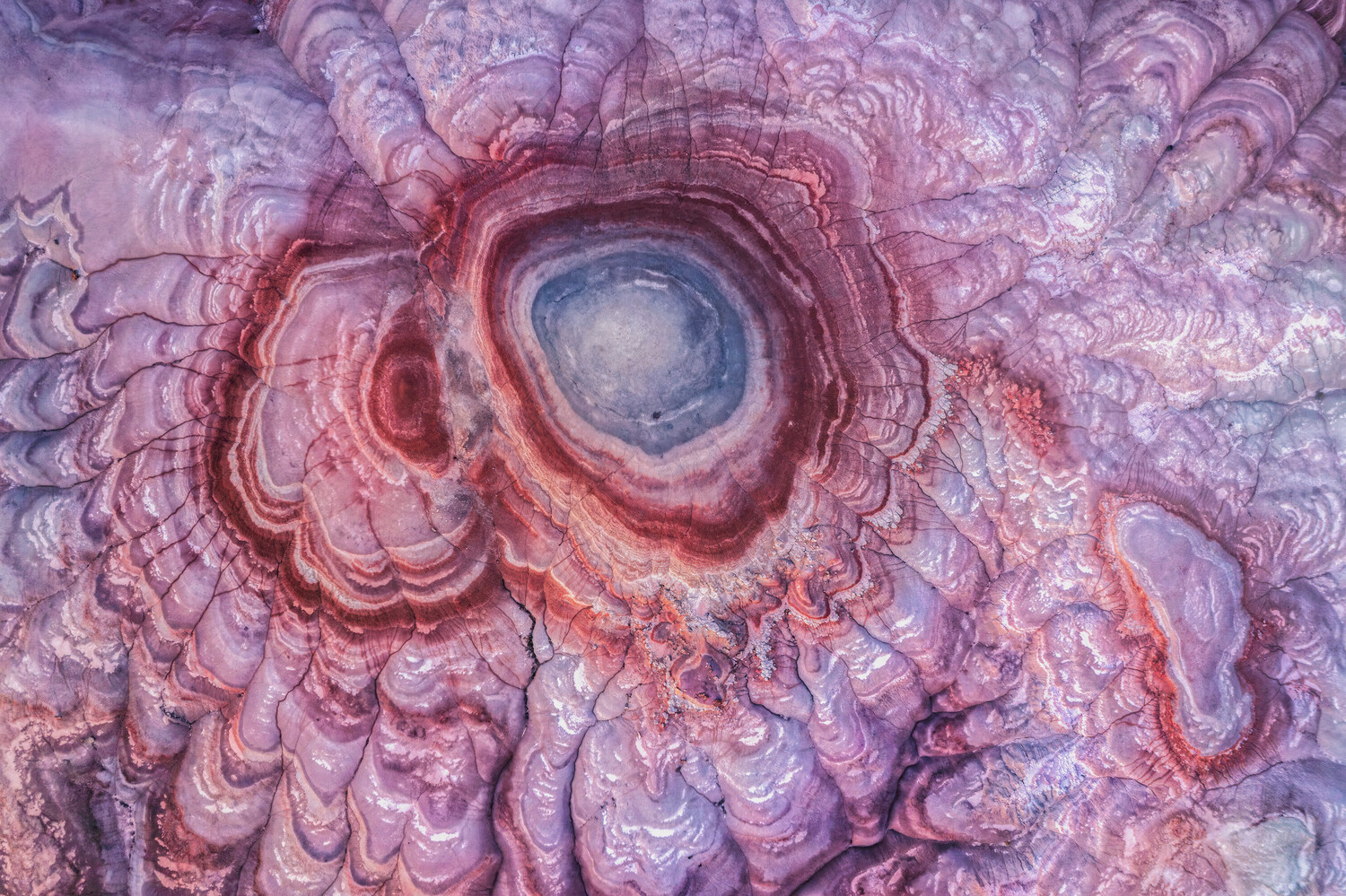 Aerial photograph of concentric circular geological formations with radiating ridges in shades of purple, pink, and blue