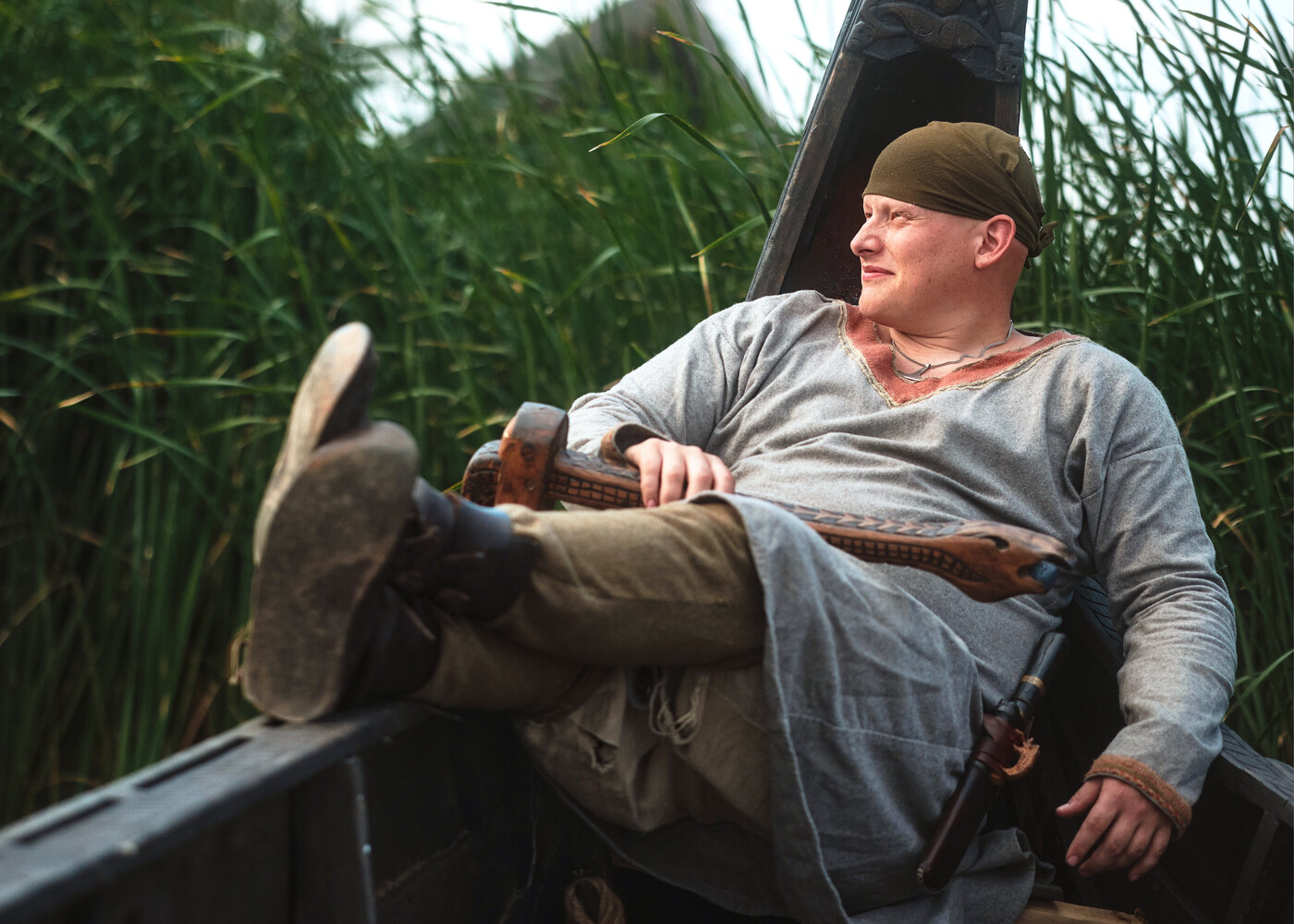 Man in casual attire relaxing in a boat with feet up, surrounded by marsh grass and reeds