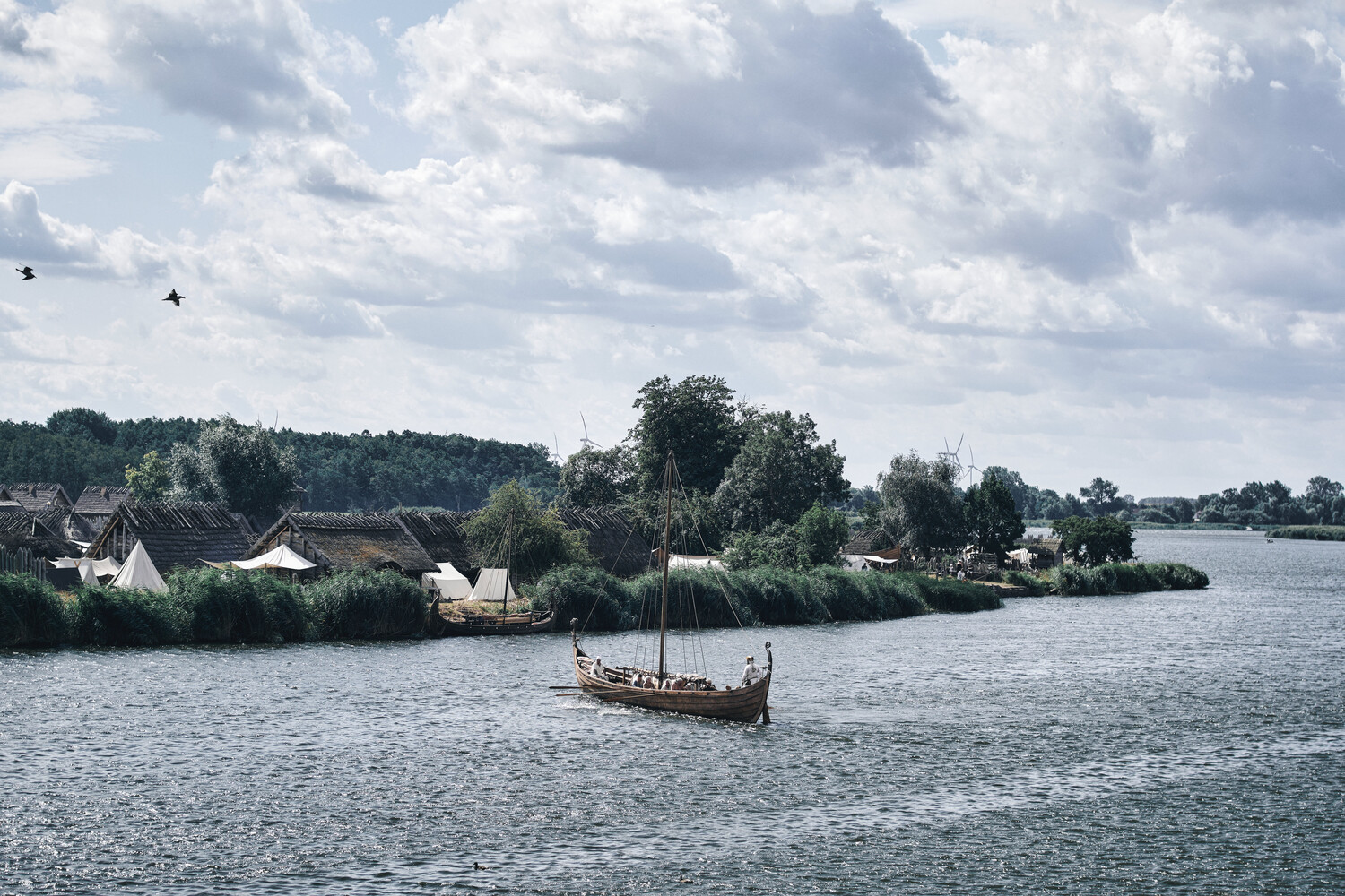 Wooden boat on calm water with riverside village and trees in background