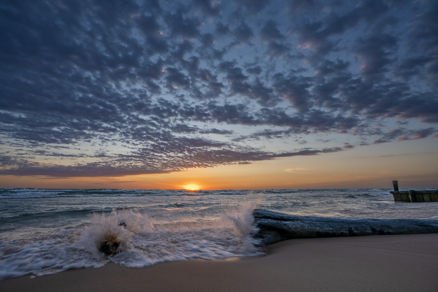 Ocean waves rolling onto sandy beach at sunset with dramatic cloud-filled sky