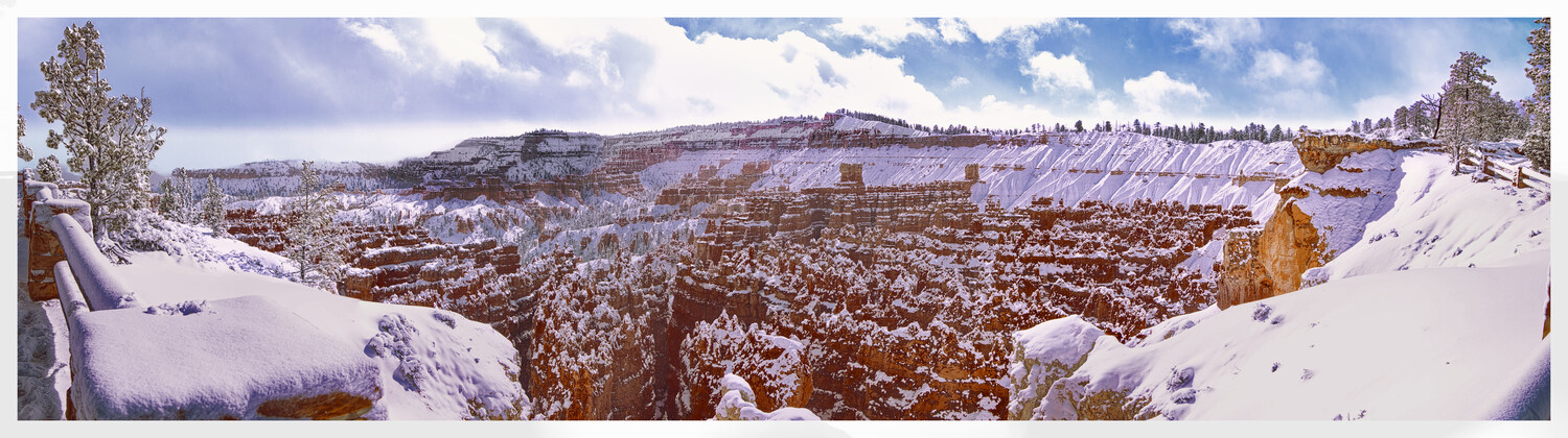Snow-covered hoodoos and canyon walls in winter landscape with scattered pine trees