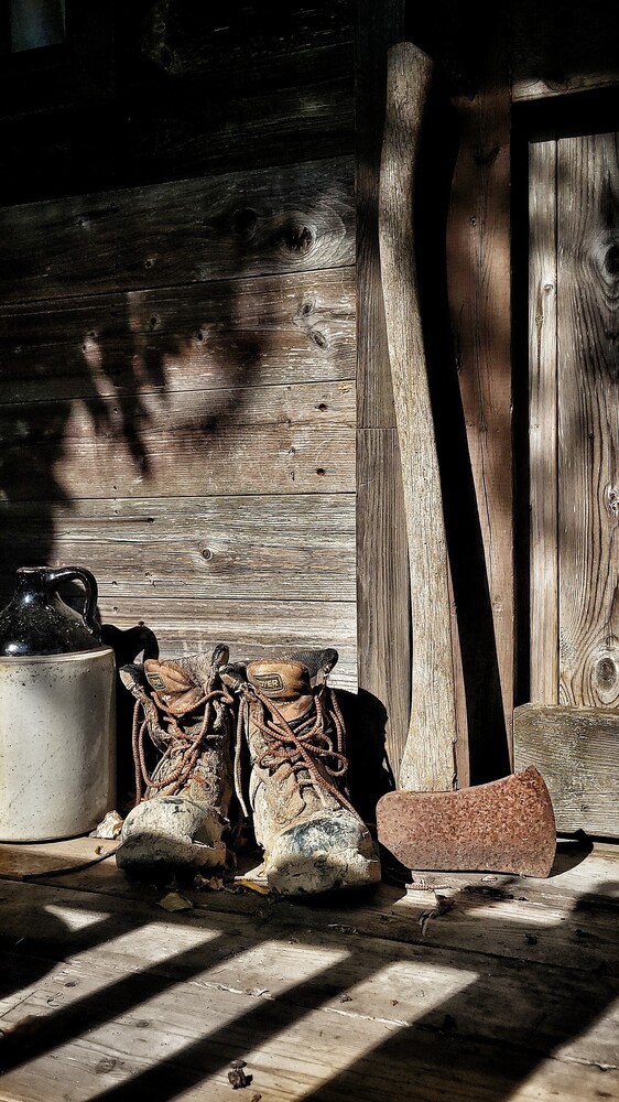 Worn leather boots and gardening tools casting shadows on weathered wooden surface