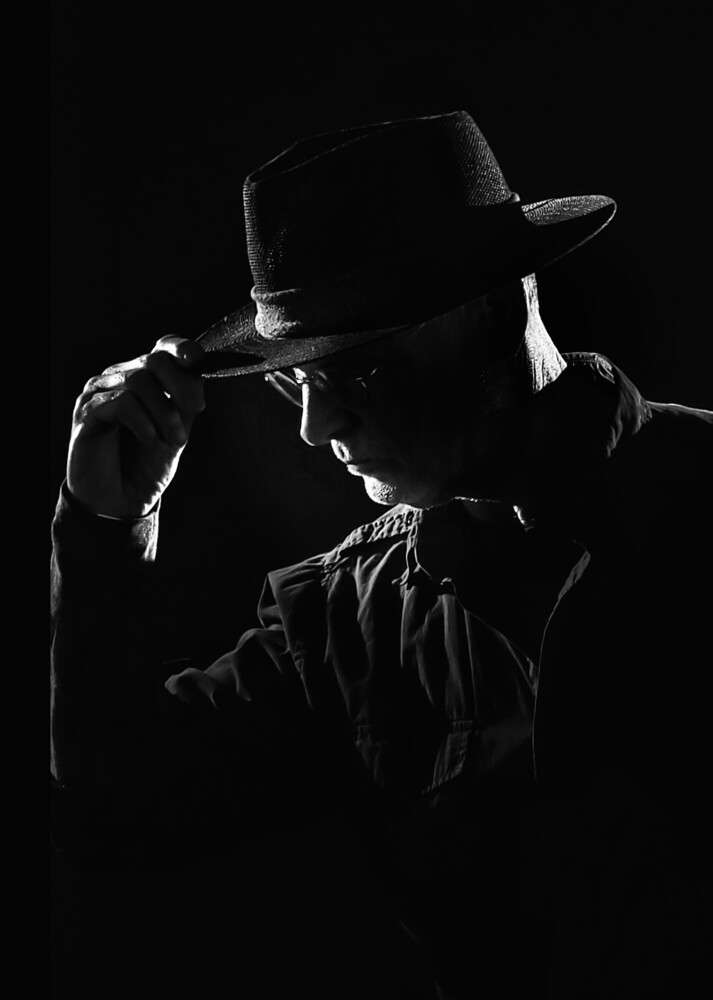 Silhouetted figure in fedora hat playing harmonica against black background