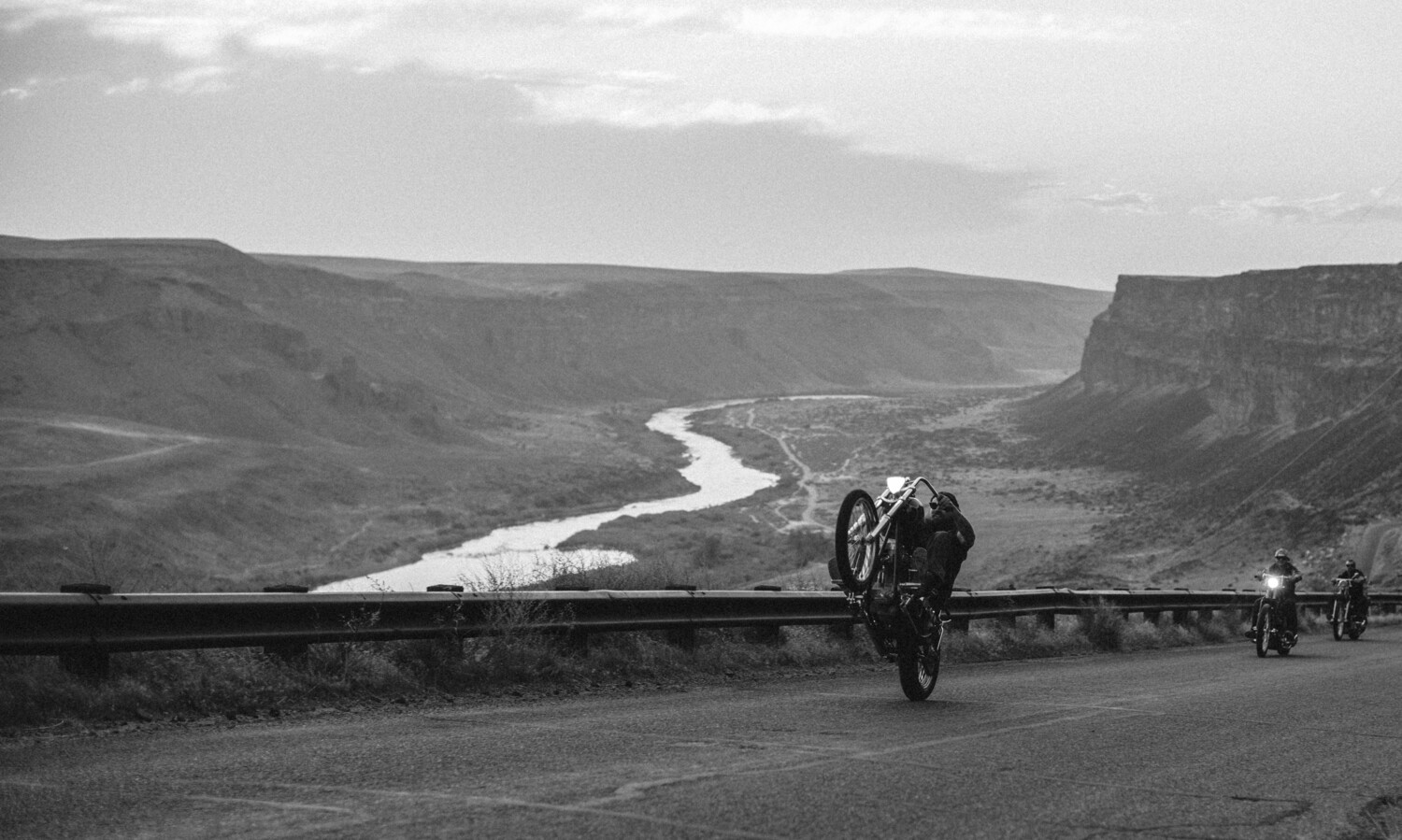 Motorcyclist riding on a curved mountain road overlooking a winding river valley