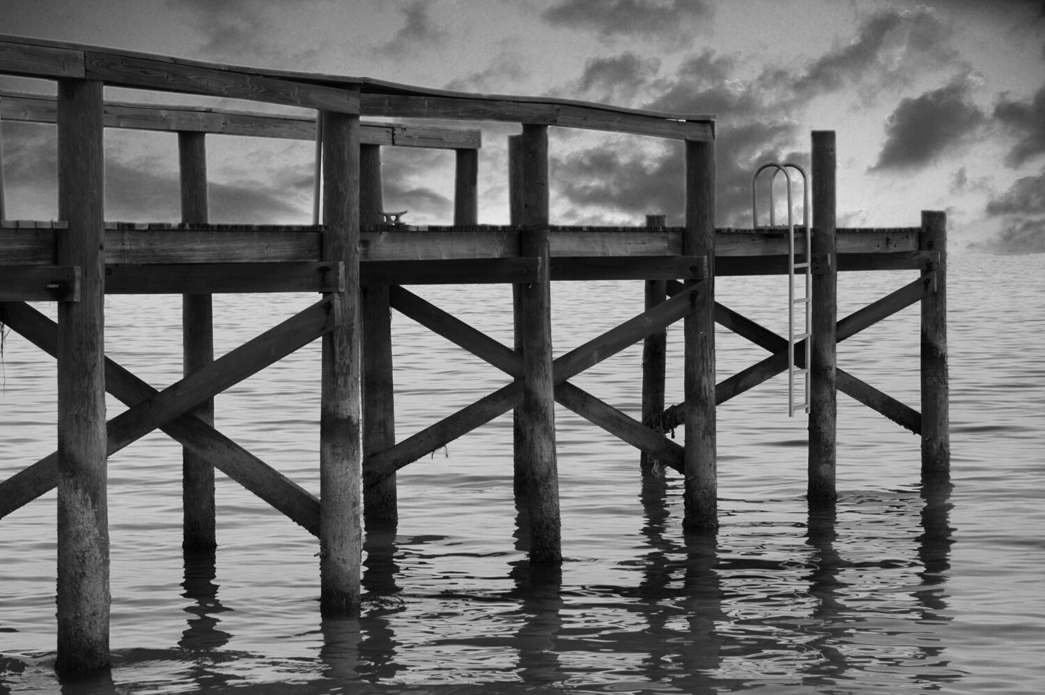 Wooden pier pilings extending into calm water under dramatic cloudy sky