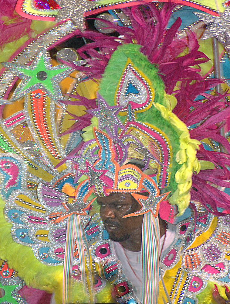 Person wearing vibrant pink and lime green patterned outfit with ornate headdress and beaded accessories