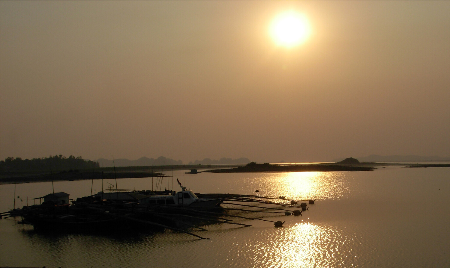 Silhouetted boats anchored in calm water at golden hour with sun reflecting across the surface