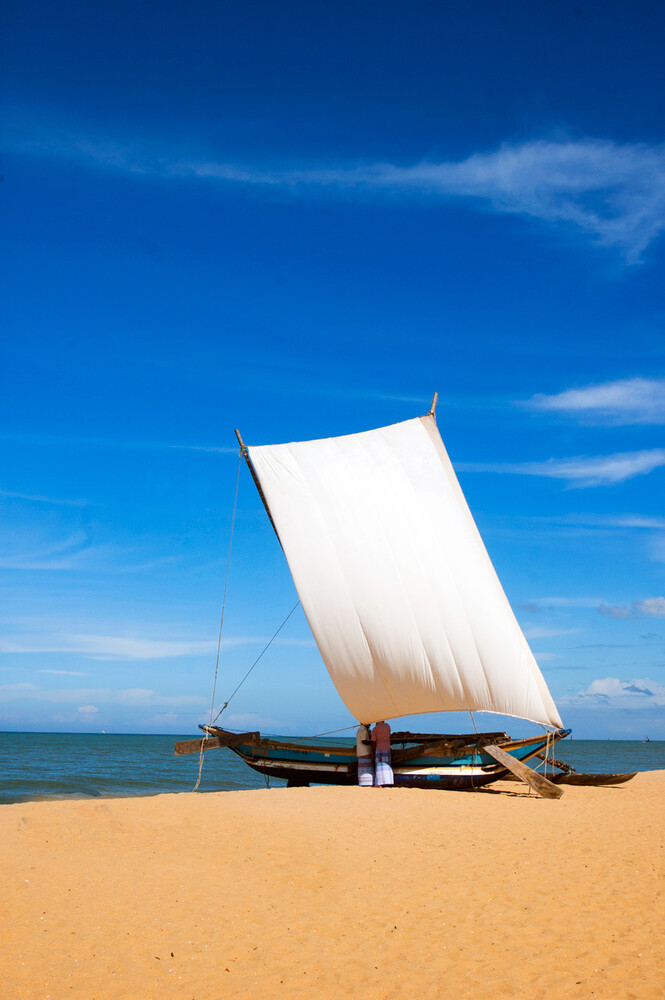 White sail on a wooden boat resting on a sandy beach under a deep blue sky, with calm sea behind it