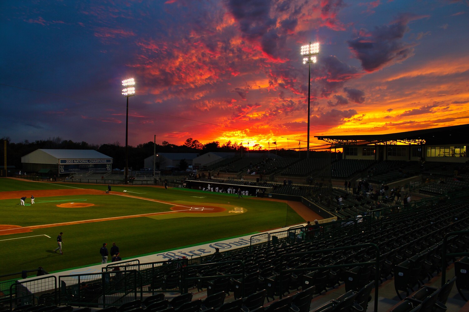 Baseball field at twilight with dramatic orange and purple sunset sky illuminated by stadium lights