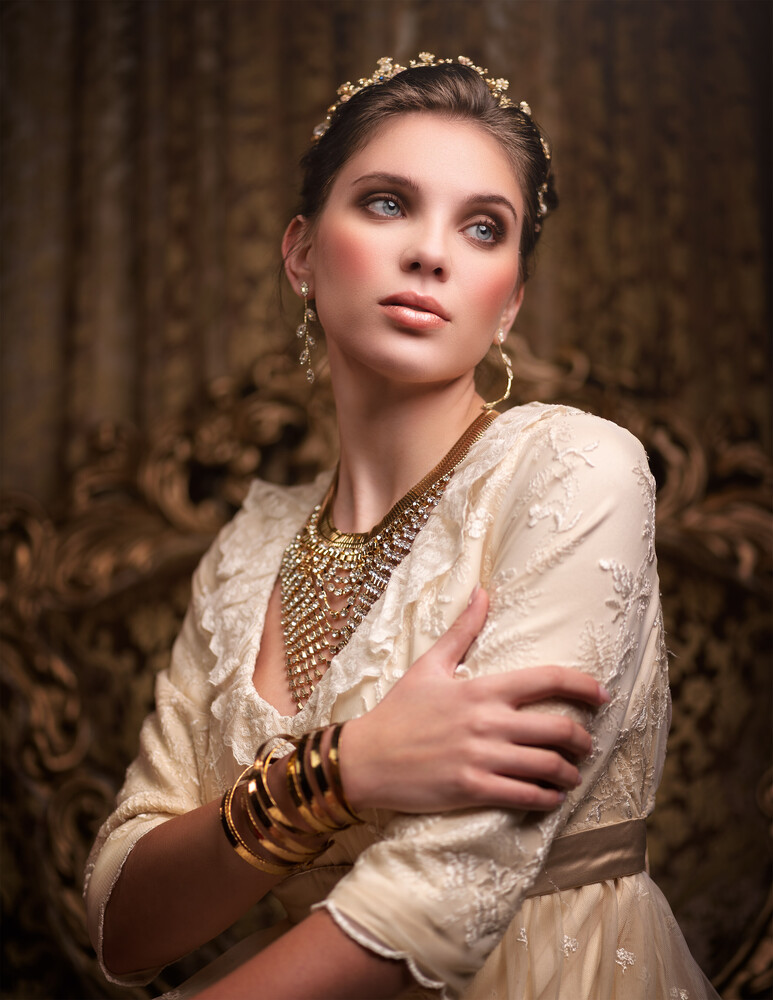 Woman in ornate period costume with tiara and jewelry gazing upward