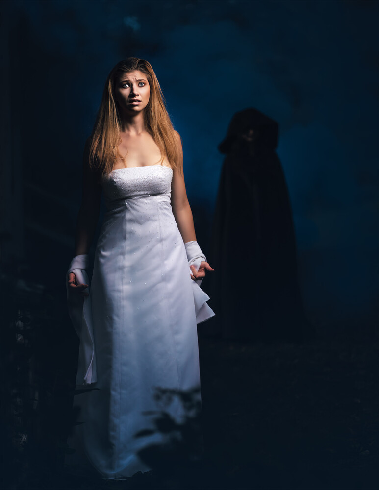 Woman in a white strapless gown and white gloves standing in a dark, blue-toned scene, with a shadowy hooded figure looming behind her.