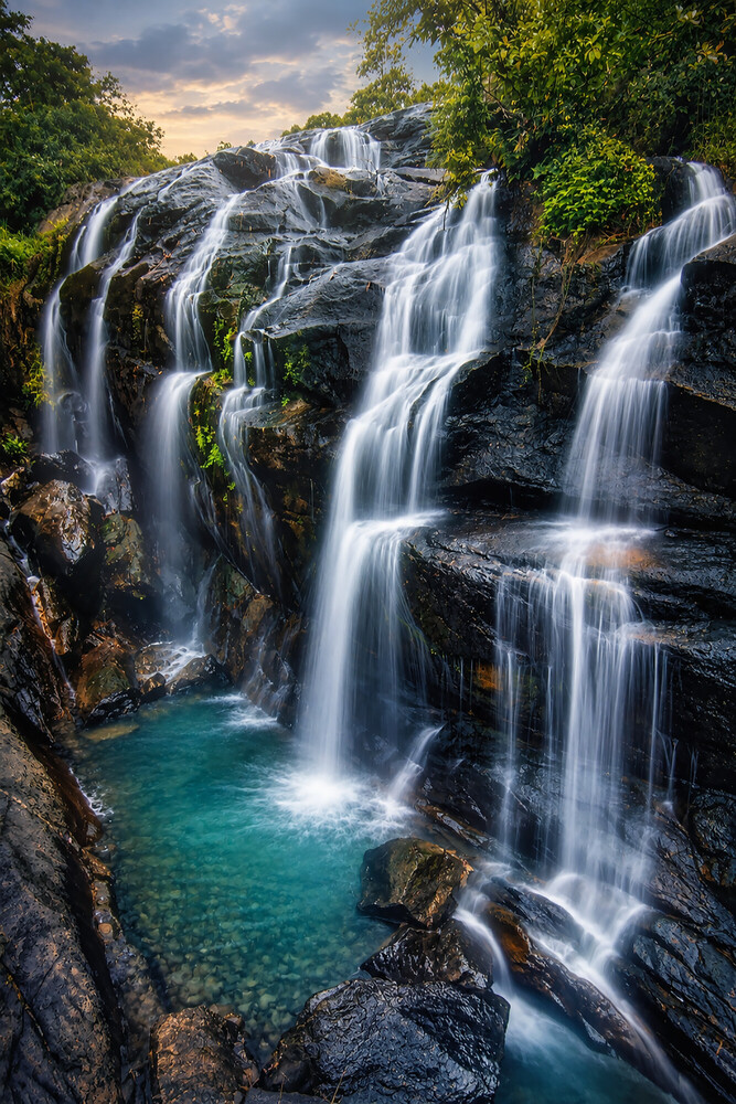 Multi-tiered waterfall cascading into turquoise pool surrounded by moss-covered rocks