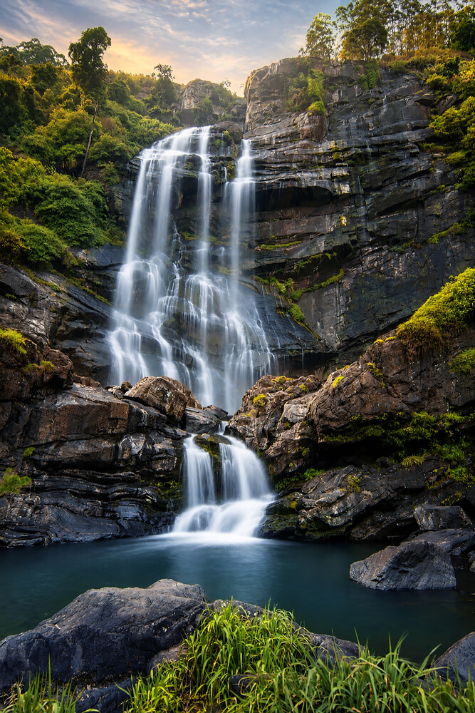 Multi-tiered waterfall cascading into an emerald pool surrounded by lush forest