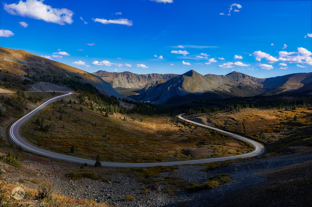 Winding mountain road curving through alpine valley beneath peaks