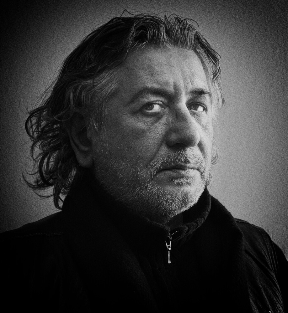 Black and white portrait of a middle-aged man with shoulder-length hair, looking directly at camera