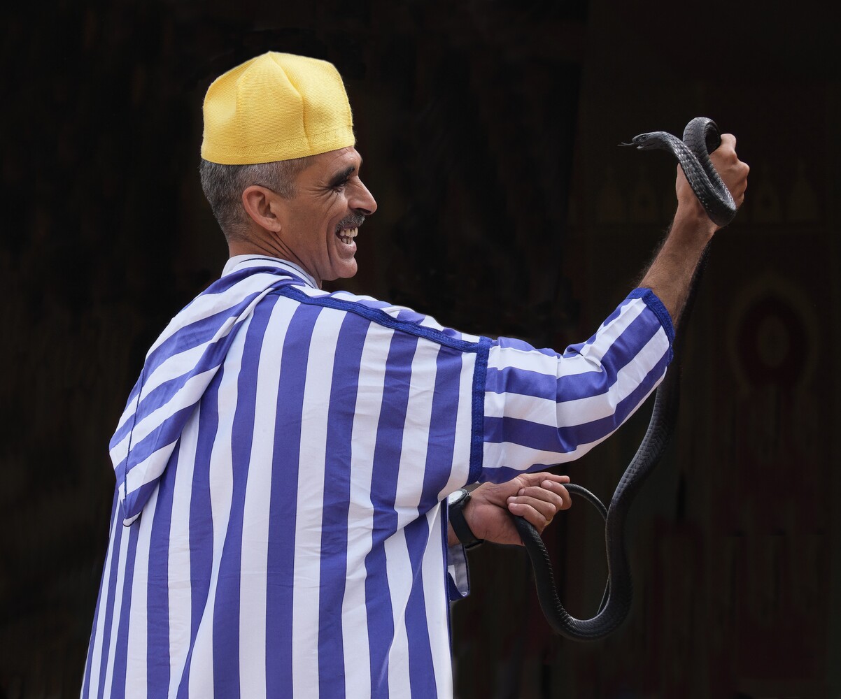 Man in blue striped shirt and yellow hard hat holding a hammer, photographed against a dark background