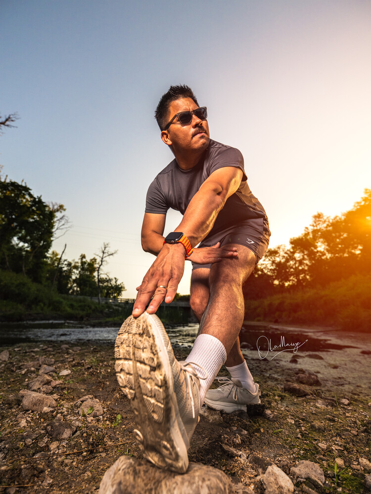 Male runner stretching his leg on a rocky surface during golden hour