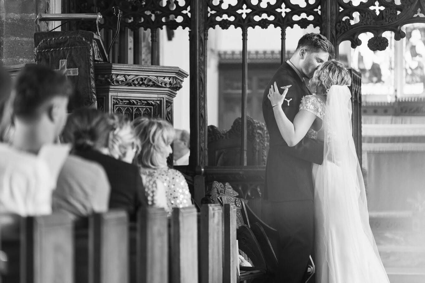 Bride and groom kissing at altar with guests watching through ornate church doors
