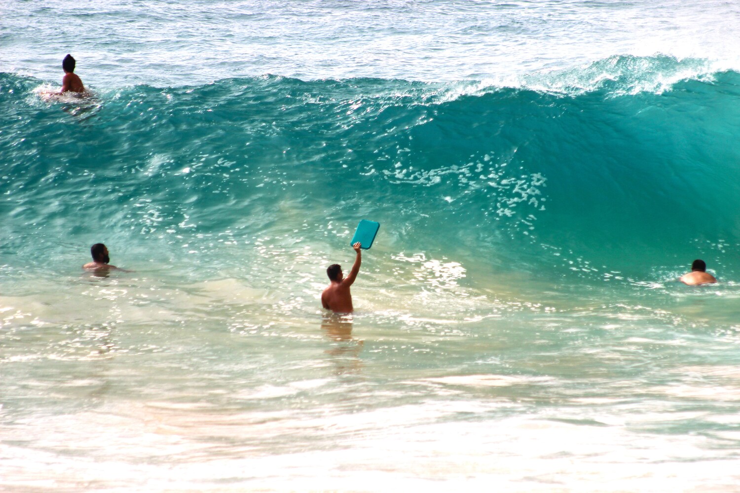 Swimmers and a snorkeler in turquoise ocean waves with white foam and sandy shore