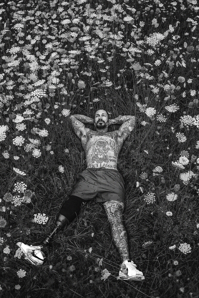 Man lying in grass surrounded by white flowers, shot from above in black and white