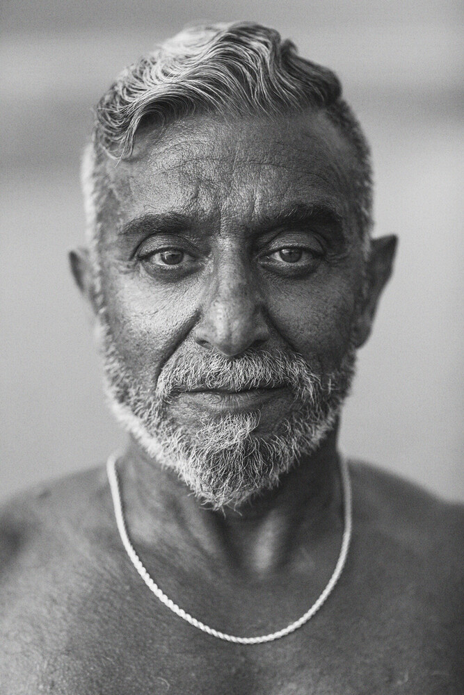 Portrait of an older man with gray hair and beard wearing a light-colored crew neck shirt